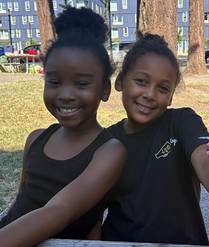 An image of 2 kids in black shirts smiling. 