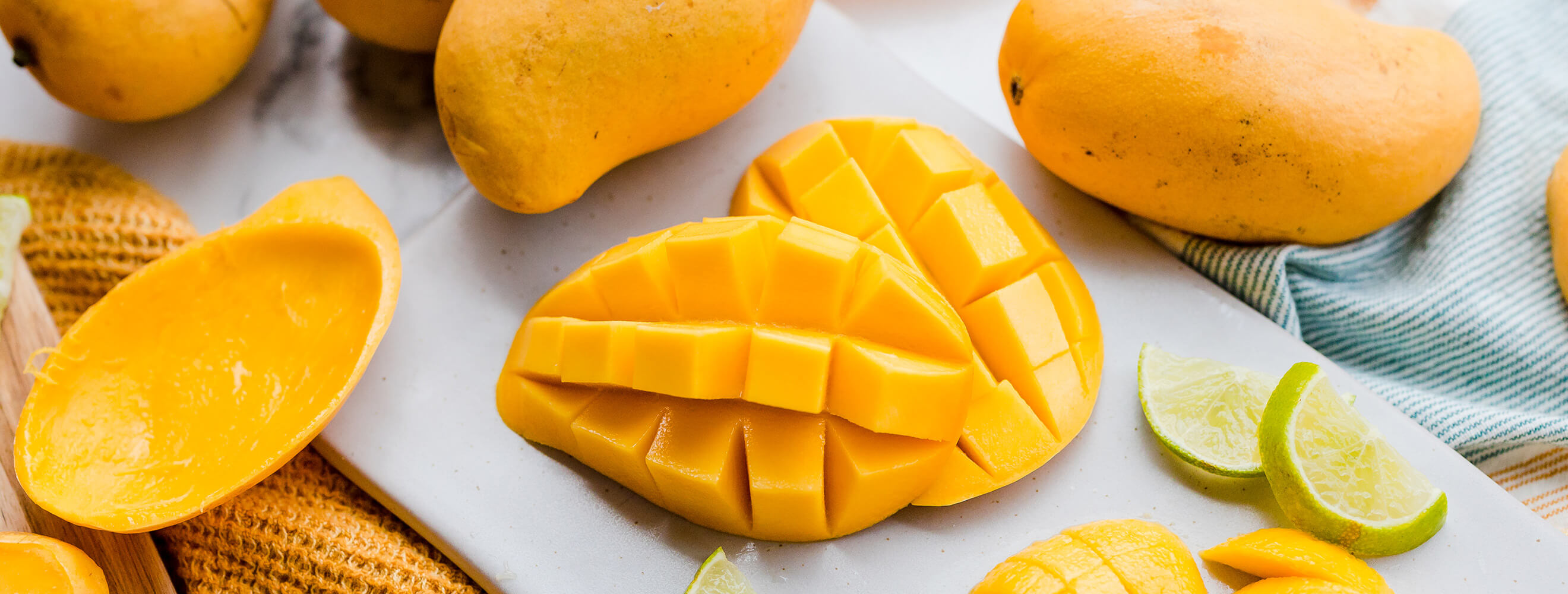 An image of sliced mango still attached to the peel, with a few whole fruits around it. 