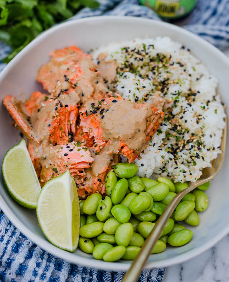 A bowl of rice with baked salmon, rice, and steamed edamame toped with New Seasons Sesame Noodle Sauce.