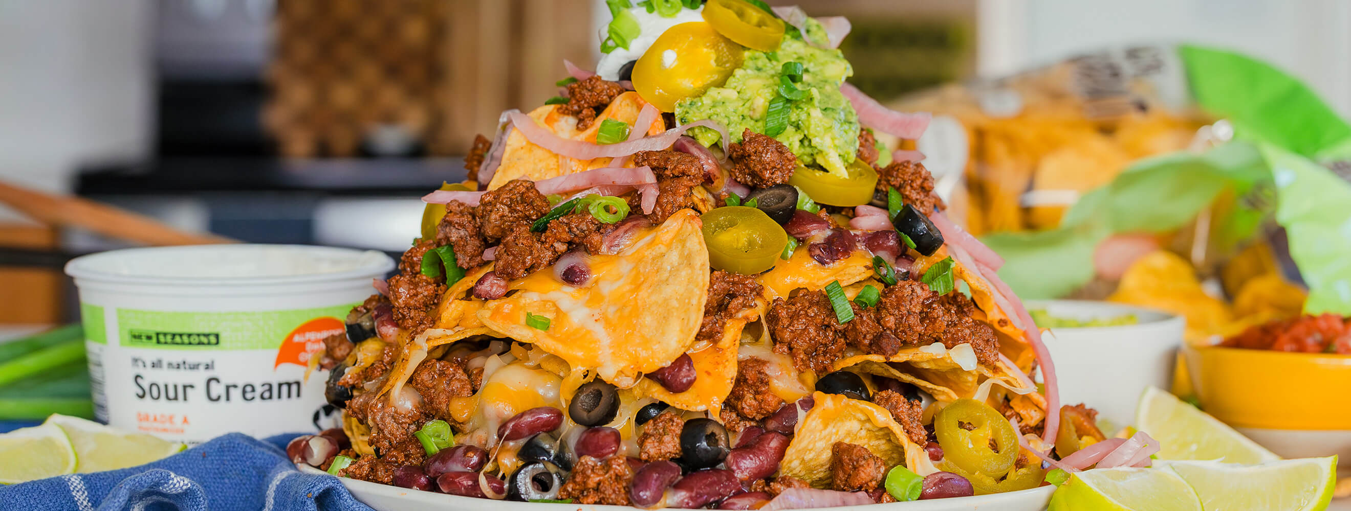 a plate with nachos piled high with tortilla chips, ground beef, cheese, shredded lettuce and sourcream