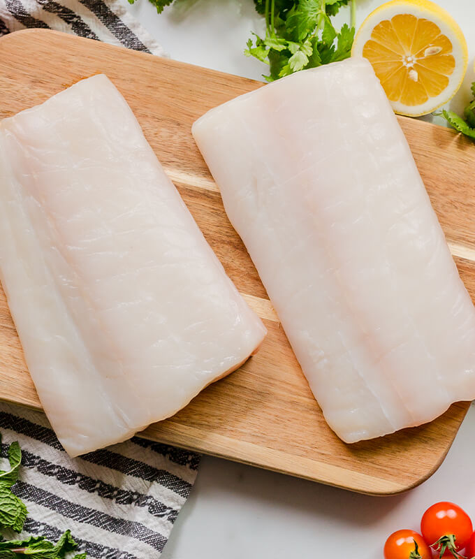 Top down image of two pieces of halibut on a cutting board.
