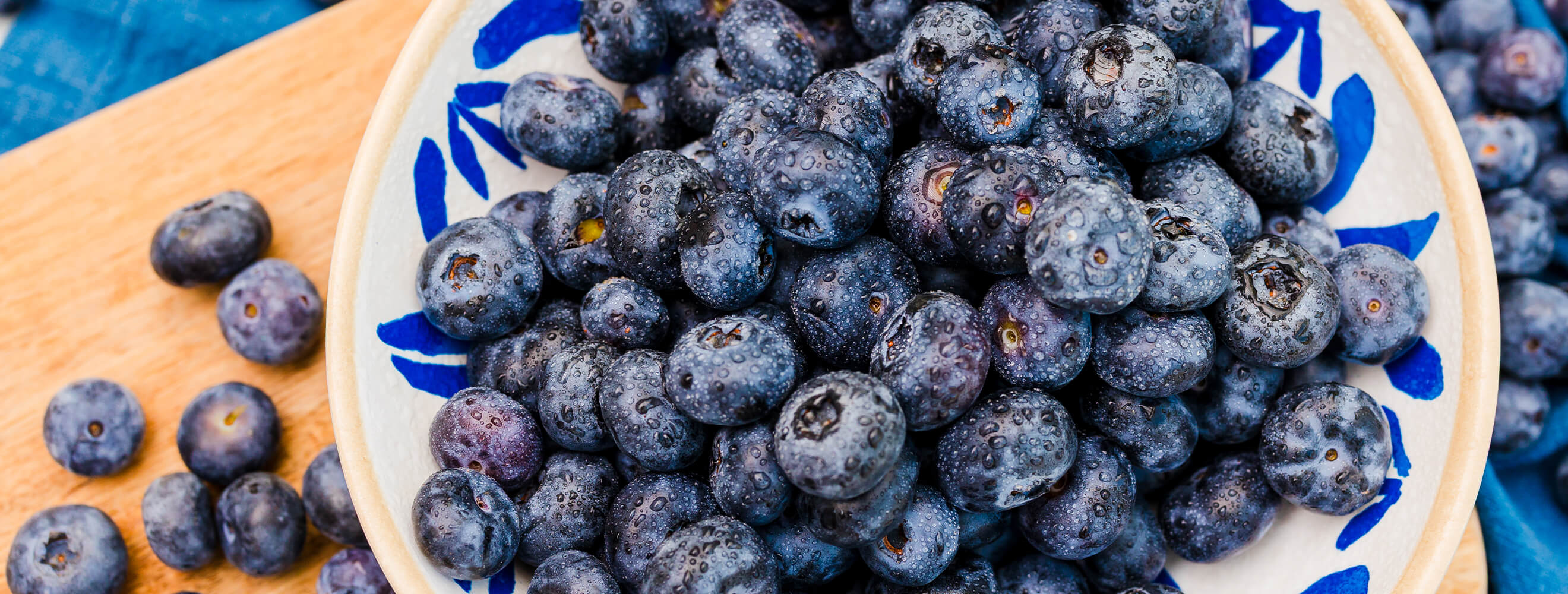 A top down image of a bowl of blueberries on a wooden board. 