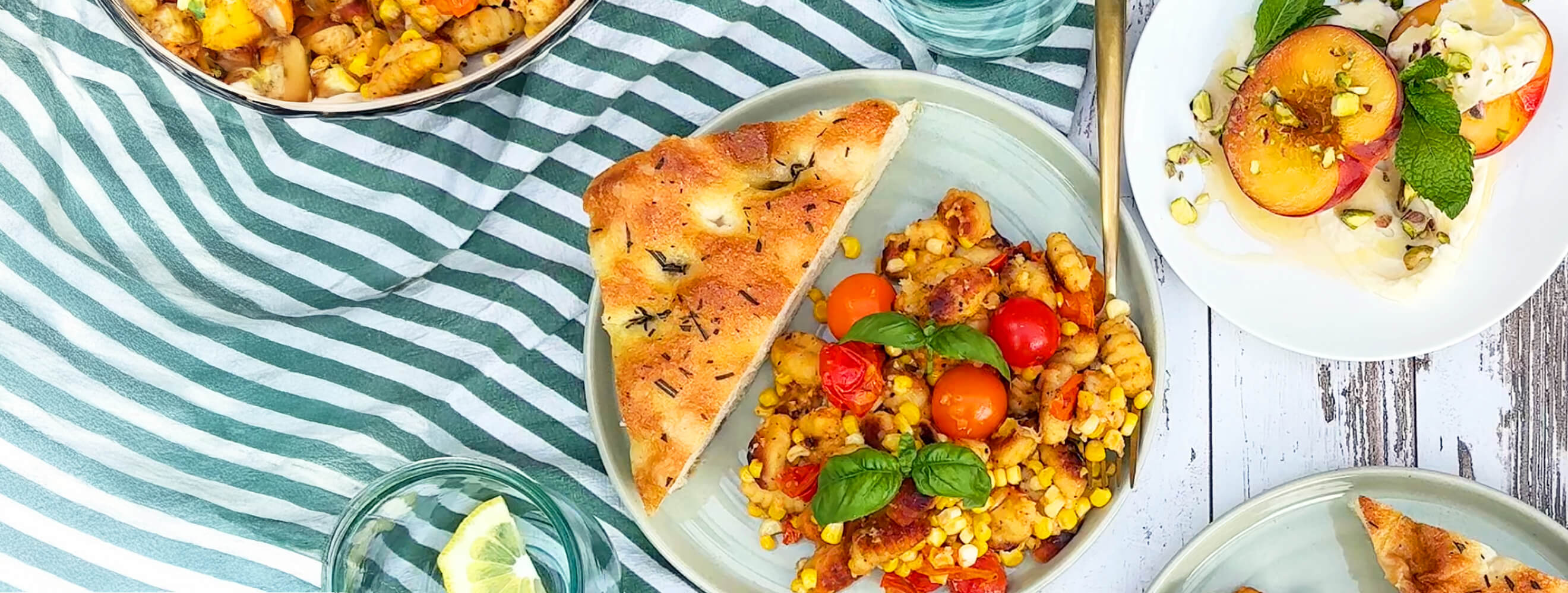 a dish of gnocchi with corn and cherry tomatoes served with focaccia bread and a peach dessert