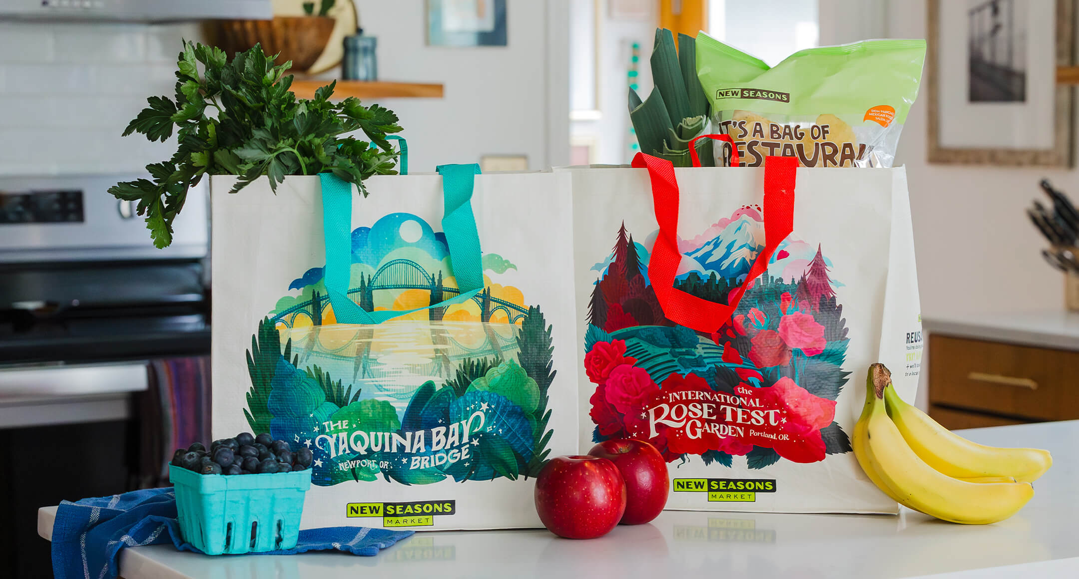 Reusable grocery bags sitting on a counter featuring artistic depictions of Oregon land marks on the side.