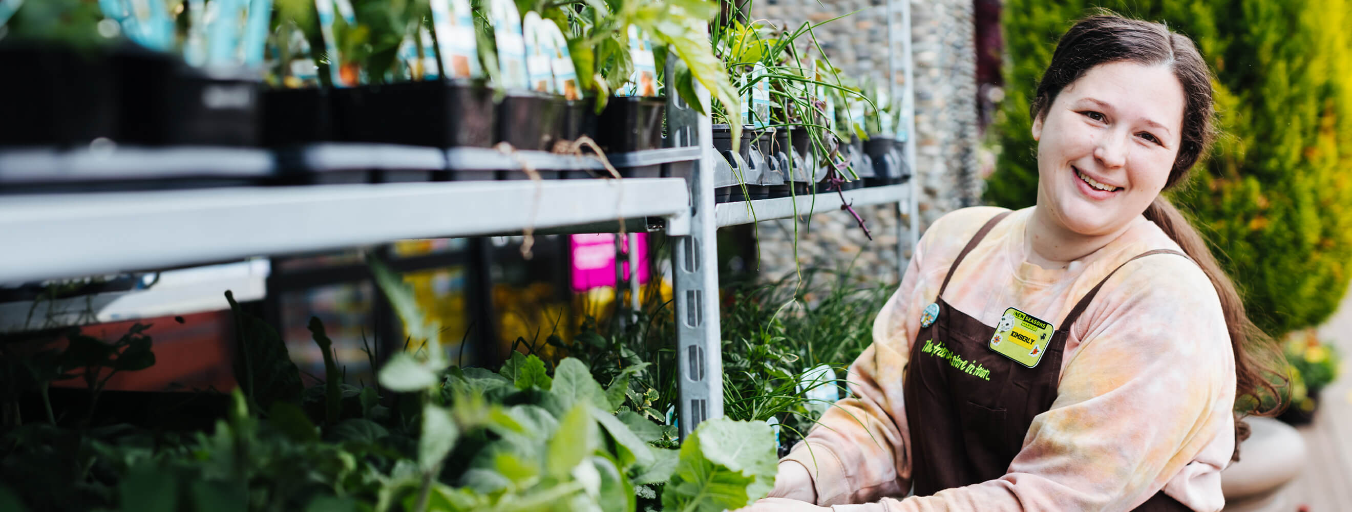 Smiling staff member tending to plants outside at a New Seasons Market location.