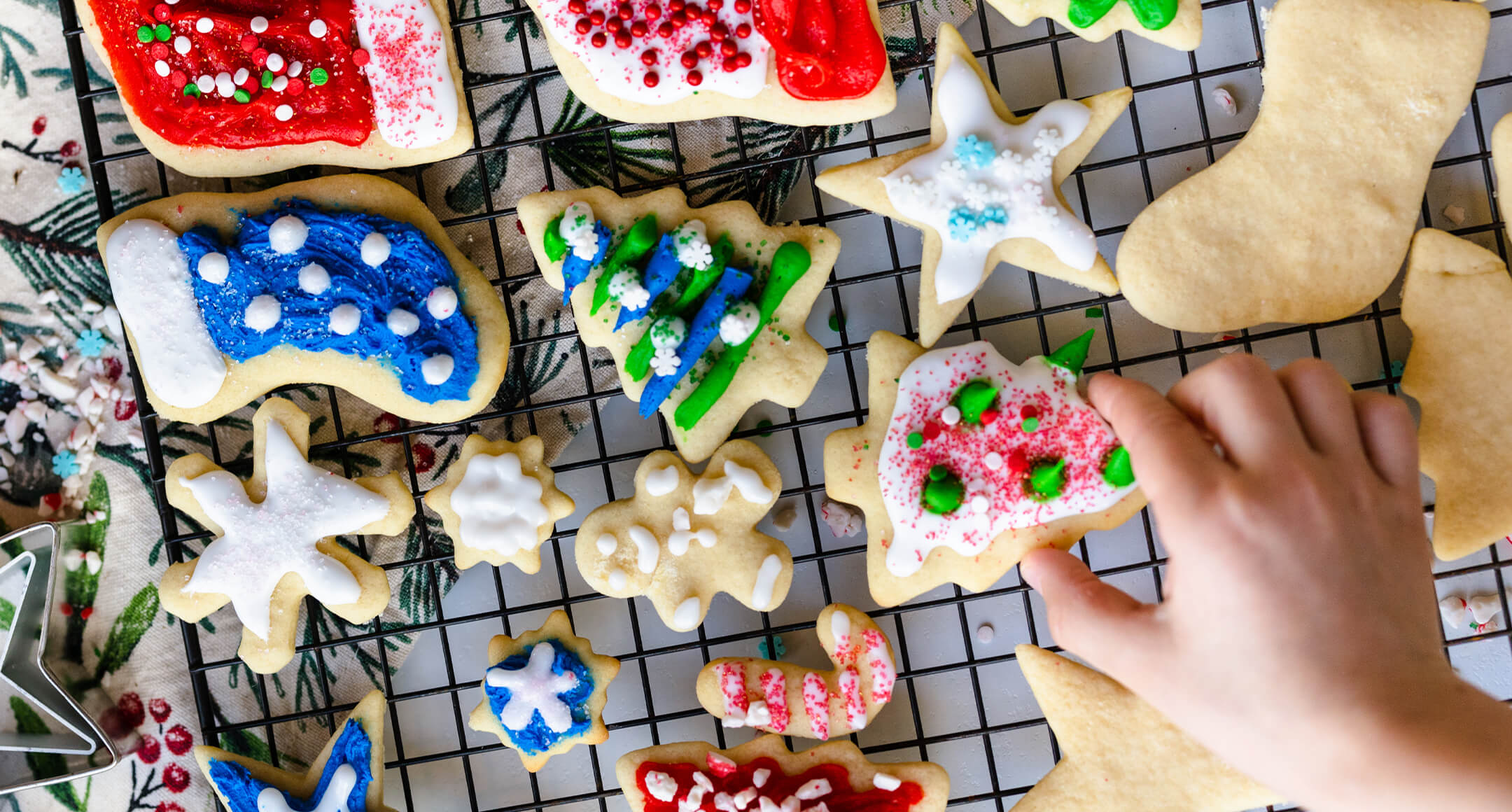 Holiday cookies being decorated on a cooling rack