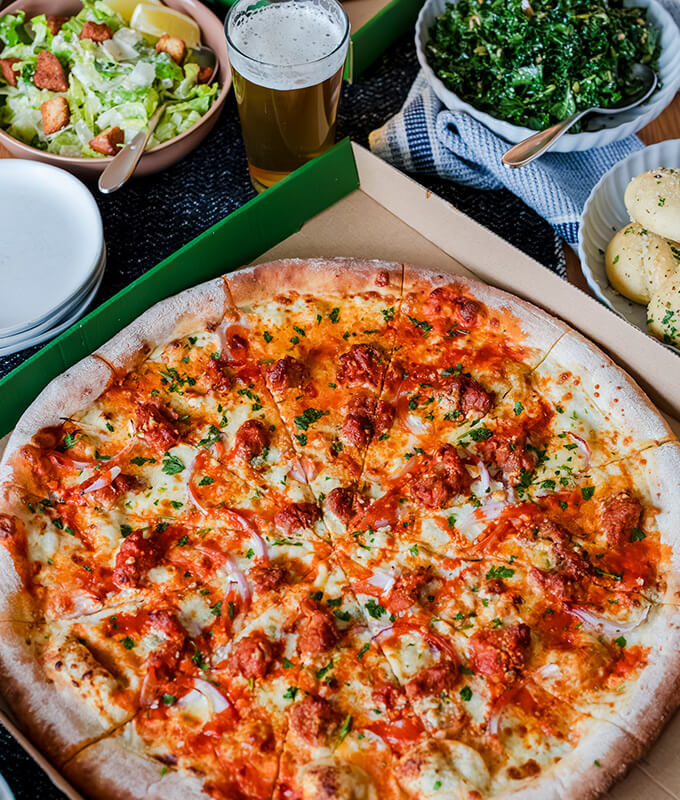 Top down image of a sliced pizza with bowls of salad around it.