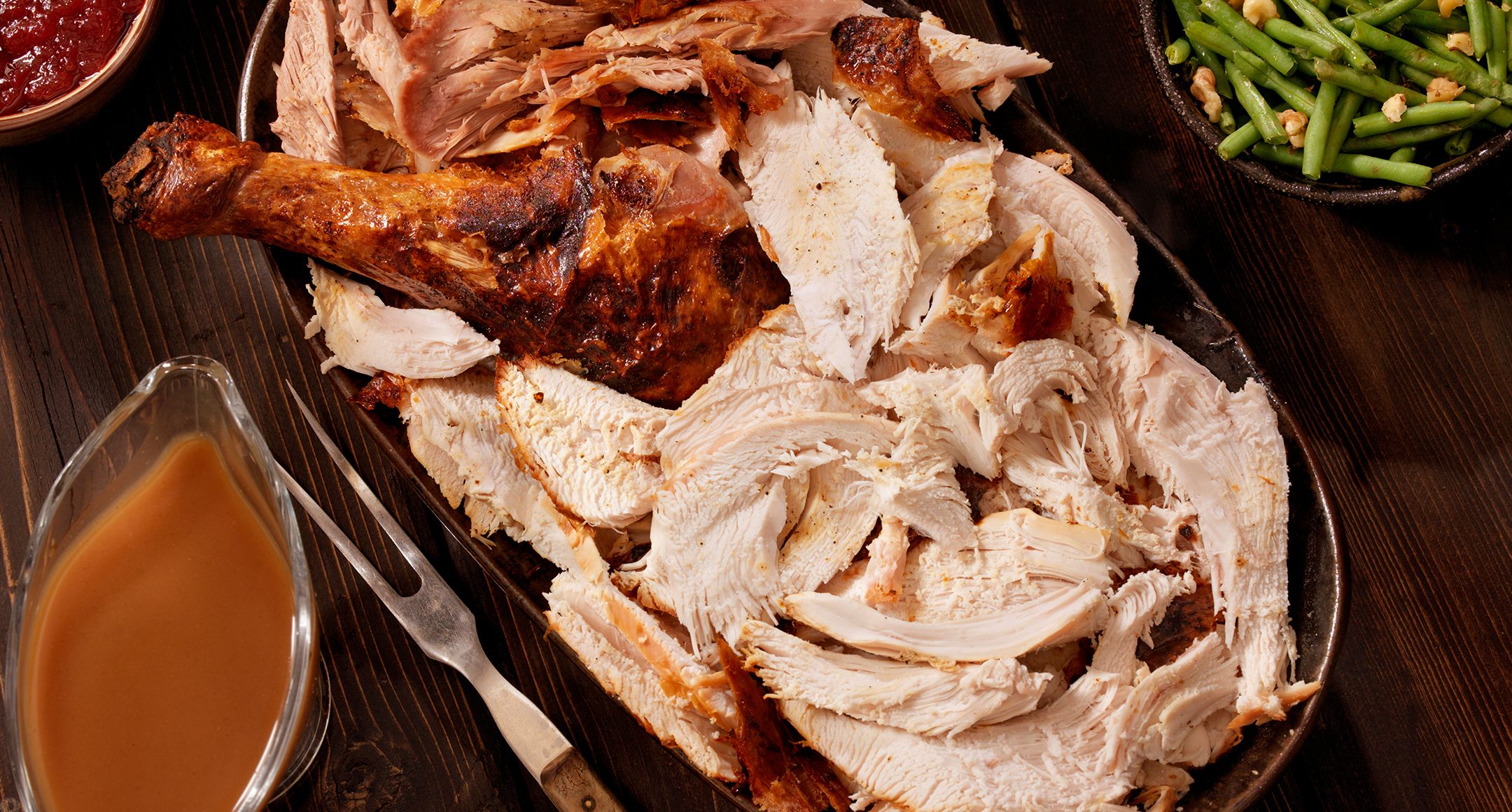 Carved turkey on a serving tray with a side of gravy. 