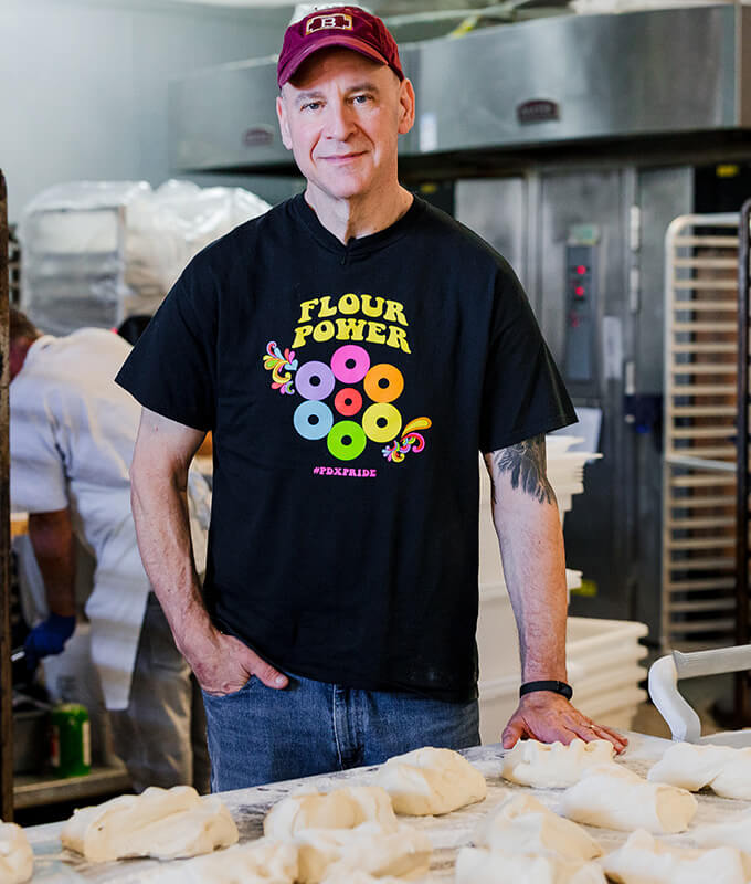 a smiling person standing in a commercial kitchen in front of pizza dough