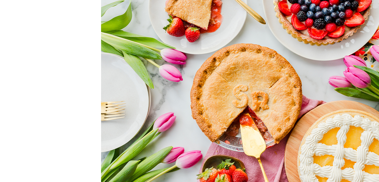 Top down image of an assortment of pies with strawberries, blueberries, and flowers