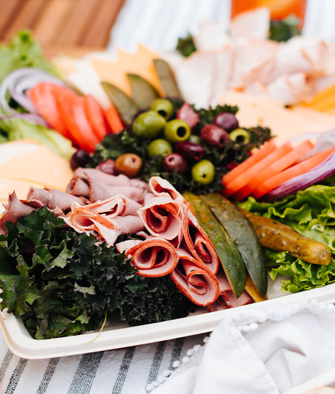 An image of a plate of food including olives, pickles, tomatoes, lettuce, and sliced meat.