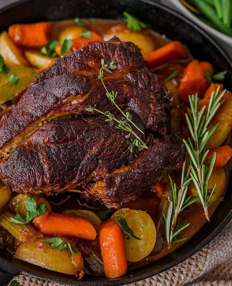 Chuck roast in a pan with carrots, potatoes and herbs