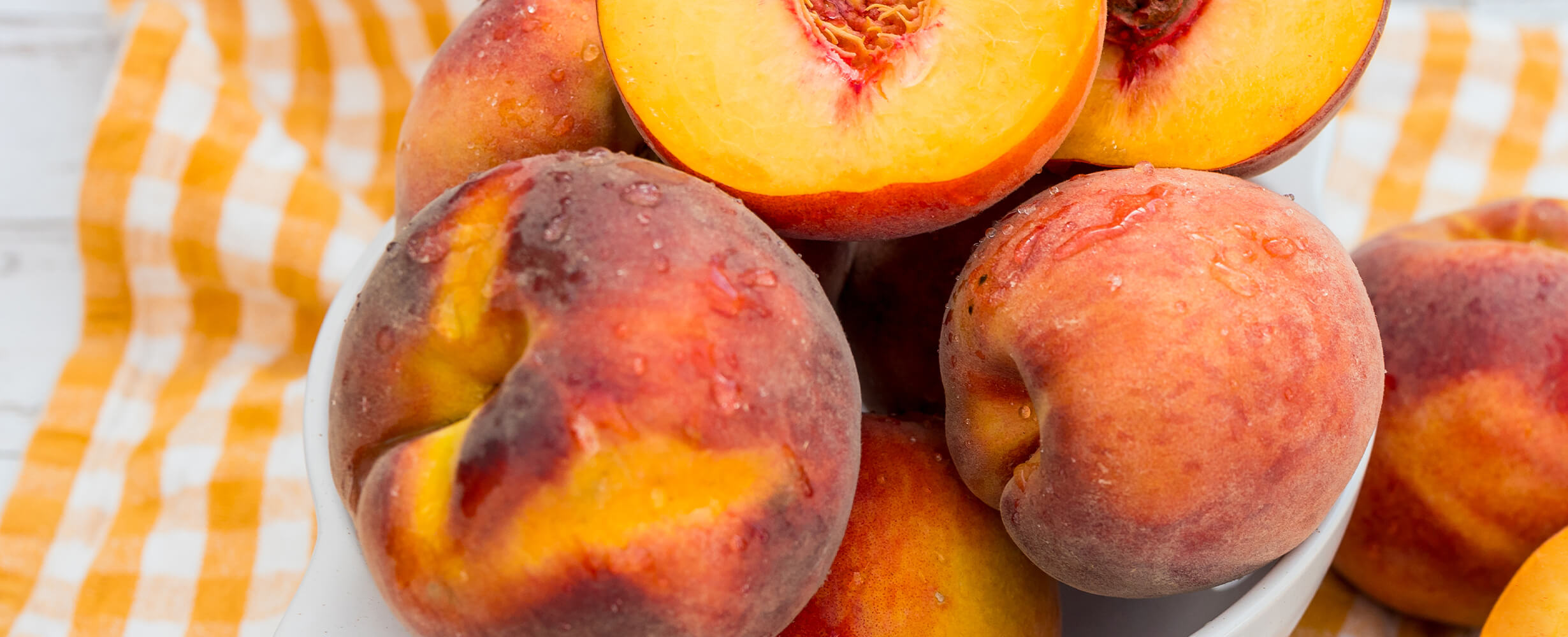 A shot of a bowl of peaches, some cut in half. 