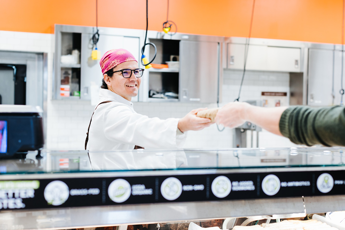 New Seasons meat department member smiling and handing product to a customer