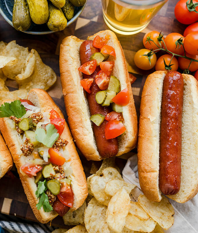 three hot dogs in buns with different toppings in a game day scene with chips and pickles