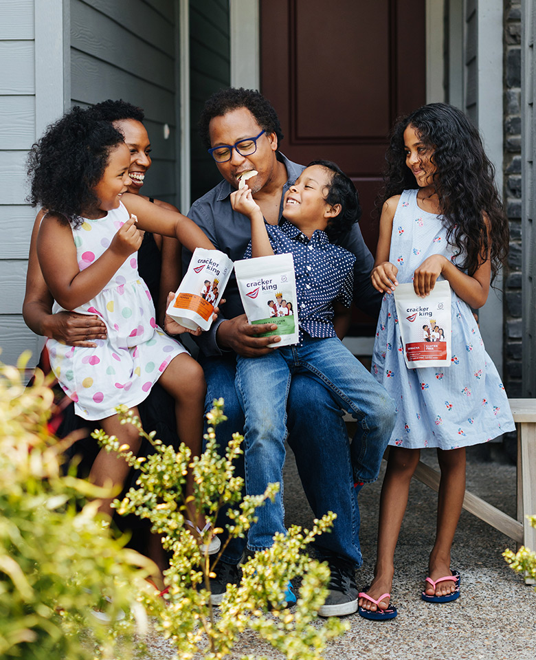 Jovani Prince of The Cracker King with 3 children holding bags of Cracker King snacks