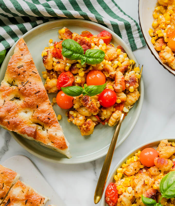 a plate with a slice of foccacia, and a corn and tomato salad topped with basil.
